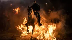 Seorang pria menunggangi kuda melewati api unggun selama festival Luminarias di San Bartolome de Pinares, Spanyol, Rabu (16/1). Acara keagamaan ini bertujuan untuk menyucikan binatang peliharaan dan ternak mereka. (AP/Felipe Dana)