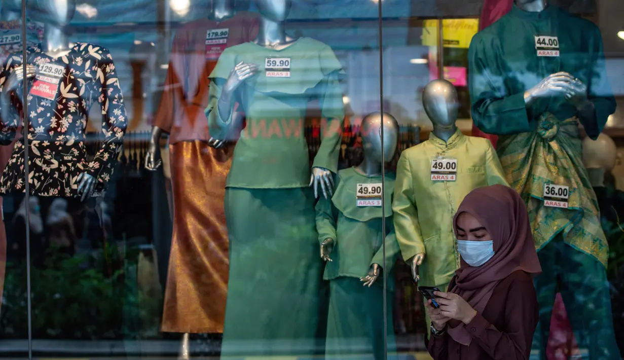 Seorang wanita mengenakan masker sebagai tindakan pencegahan Covid-19 melihat ponselnya di depan sebuah toko yang menjual pakaian budaya Malaysia yang disebut Baju Melayu dan Baju Kurung menjelang Idul Fitri yang menandai berakhirnya bulan suci Ramadan di Kuala Lumpur (13/5/2020). (AFP/Mohd Rasfan)