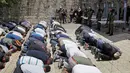 Umat muslim melakukan ibadah di depan komplek Masjid Al-Aqsa dengan penjagaan petugas perbatasan Israel di Yerusalem, Minggu (16/7). Dibukanya kembali komplek tempat suci ini untuk mengurangi kemungkinan kerusuhan yang lebih luas. (AP/Mahmoud Illean)