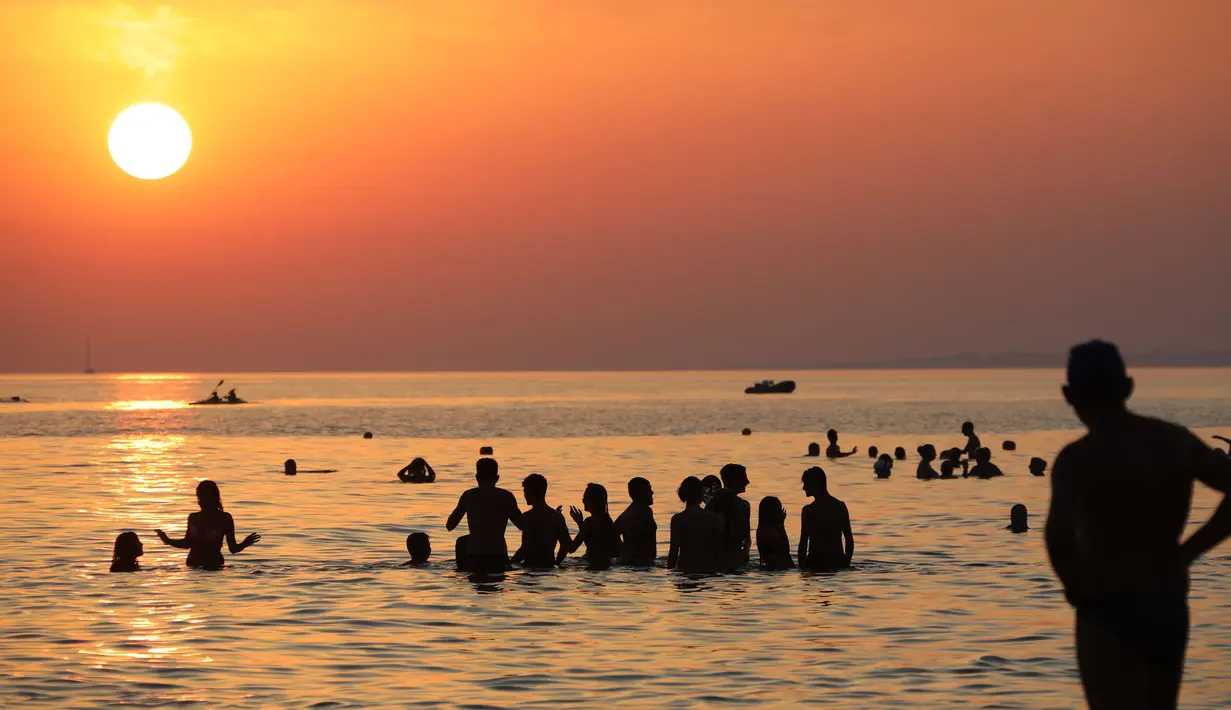 Pengunjung berenang sambil menikmati pemandangan matahari terbenam di Pantai Santa Maria Del Focalo, Pulau Sisilia, Italia, 7 Agustus 2017. Pantai Santa Maria Del Focalo menjadi salah satu tujuan objek wisata favorit di Italia. (ludovic MARIN/AFP)