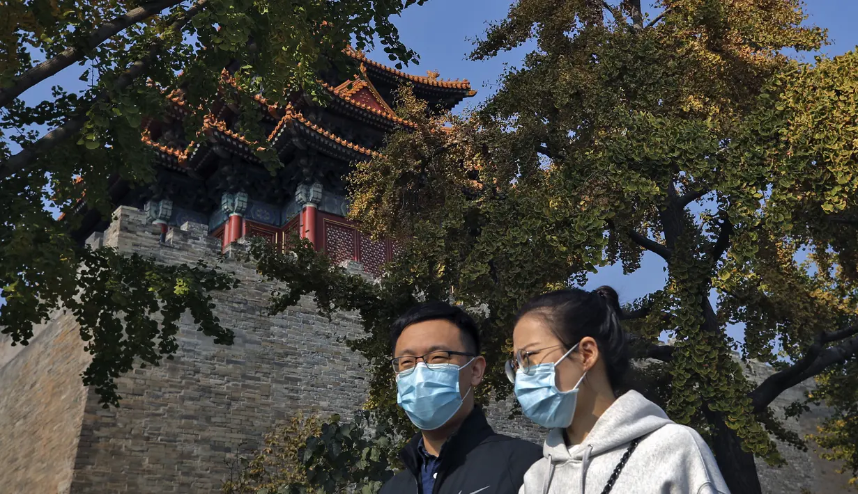 Pasangan mengenakan masker untuk mencegah penyebaran virus corona berjalan di Turret Kota Terlarang di Beijing (25/10/2020). Dengan wabah COVID-19 yang sebagian besar terkendali di dalam perbatasan China, rutinitas kehidupan sehari-hari yang normal telah mulai kembali untuk warganya. (AP Photo/Andy