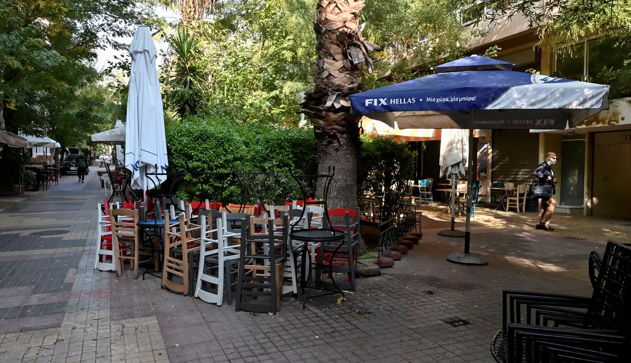 Pejalan kaki berjalan melewati restoran dan kafe yang tutup di pusat Athena, Yunani, Selasa (16/11/2021). Pemilik restoran, kafe, dan bar melakukan pemogokan selama 24 jam, memprotes aturan terkait Covid-19 dan biaya energi yang tinggi. (Louisa GOULIAMAKI / AFP)