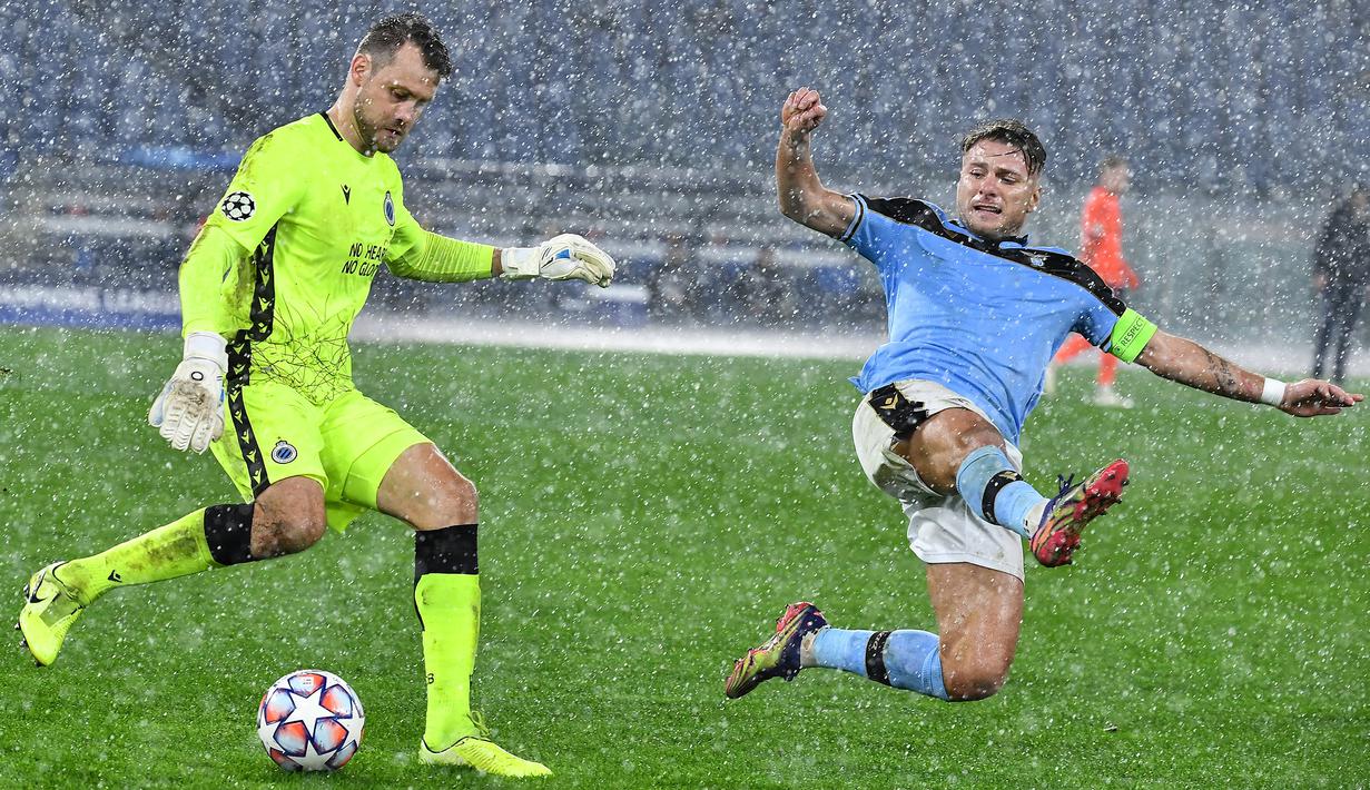 Penyerang Lazio, Ciro Immobile, berusaga merebut bola dari kiper Club Brugge, Simon Mignolet, pada laga Grup F Liga Champions di Olympic Stadium, Rabu (9/12/2020) dini hari WIB. Lazio bermain imbang 2-2 melawan Club Brugge. (AFP/Tiziana Fabi)