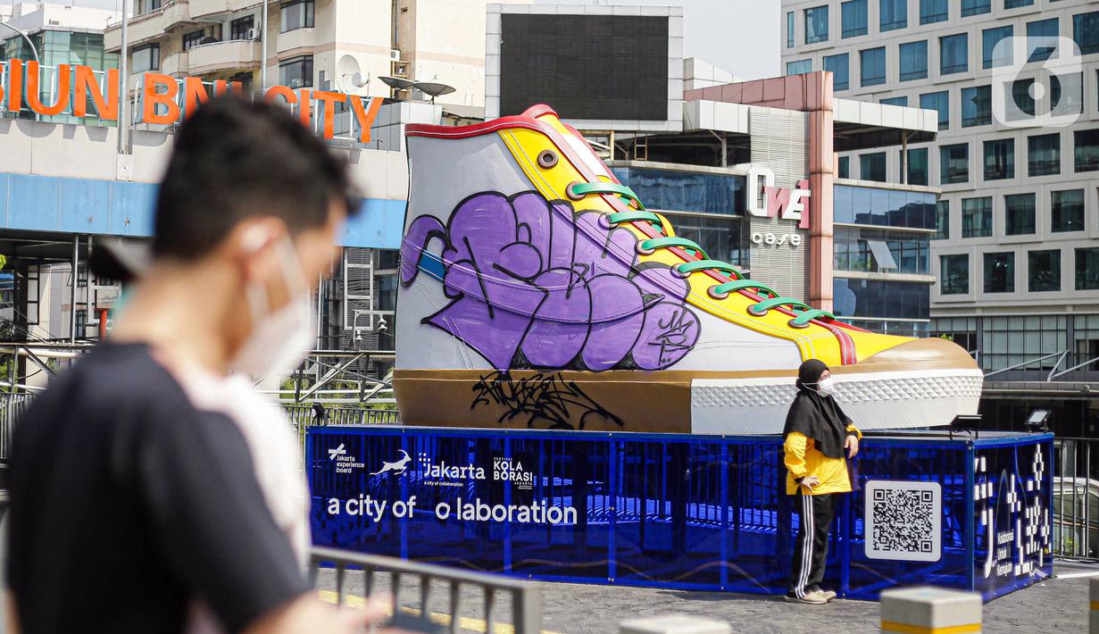 Warga berfoto di depan Tugu Sepatu, Sudirman, Jakarta, Minggu (19/9/2021). Tugu Sepatu menjadi sasaran pencoretan dengan semprotan aerosol oleh orang tak dikenal sehari usai diresmikan pada 17 September 2021. (Liputan6.com/Faizal Fanani)