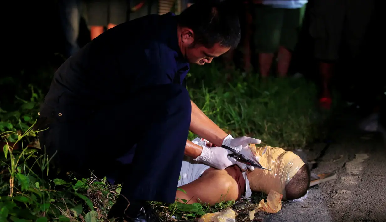 Petugas memotong lilitan lakban wajah seorang jenazah pria di sebuah jalan di kota Pasay, metro Manila, Filipina (17/11). Belakangan, banyak korban yang merupakan pecandu dan bandar di Filipina tewas dalam kondisi mengenaskan. (Reuters/Romeo Ranoco)