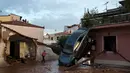 Seorang wanita berjalan dekat sebuah mobil yang terbalik akibat diterjang banjir bandang di kota industri Mandra, barat Athena, Rabu (15/11). Bencana tersebut dinyatakan sebagai banjir terparah di Yunani selama 20 tahun terakhir. (AP/Petros Giannakouris)