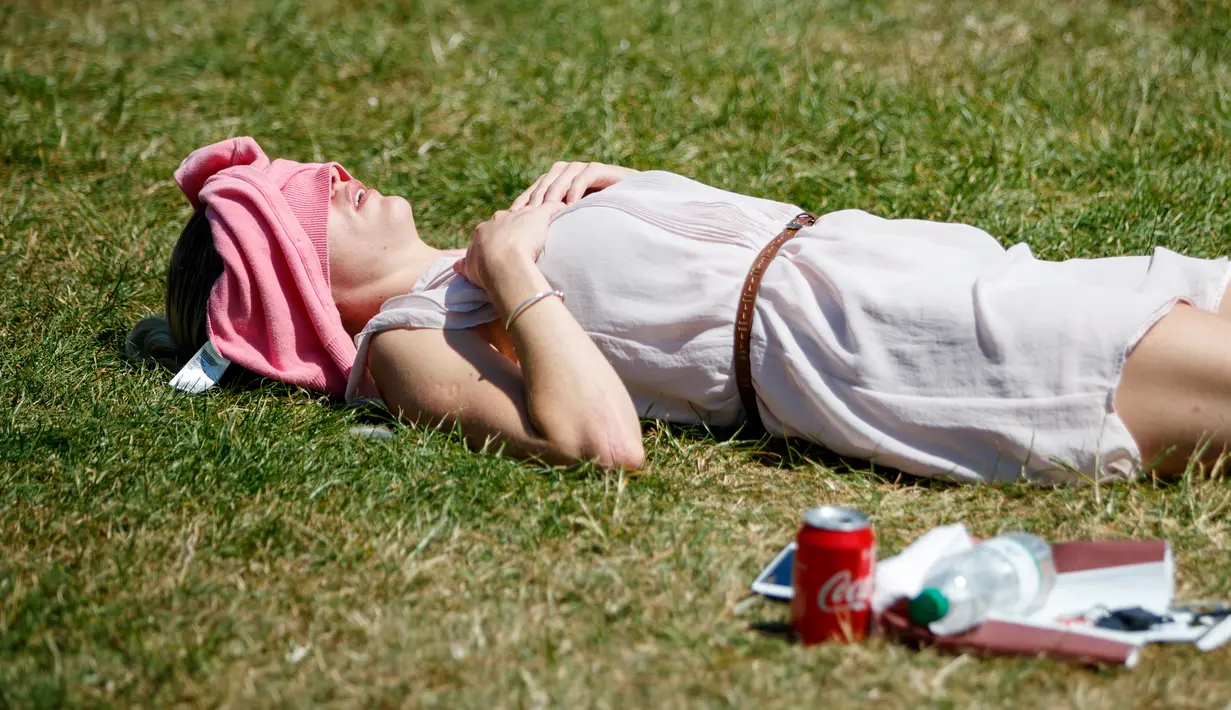 Seorang wanita Inggris berjemur di atas rumput sambil menikmati sinar matahari di Green Park, London, Senin (25/6). Pada Juli 2018, suhu di ibu kota London tercatat 29.1 derajat Celcius dan diprediksi akan mencapai 30 derajat Celcius. (AFP/Tolga Akmen)