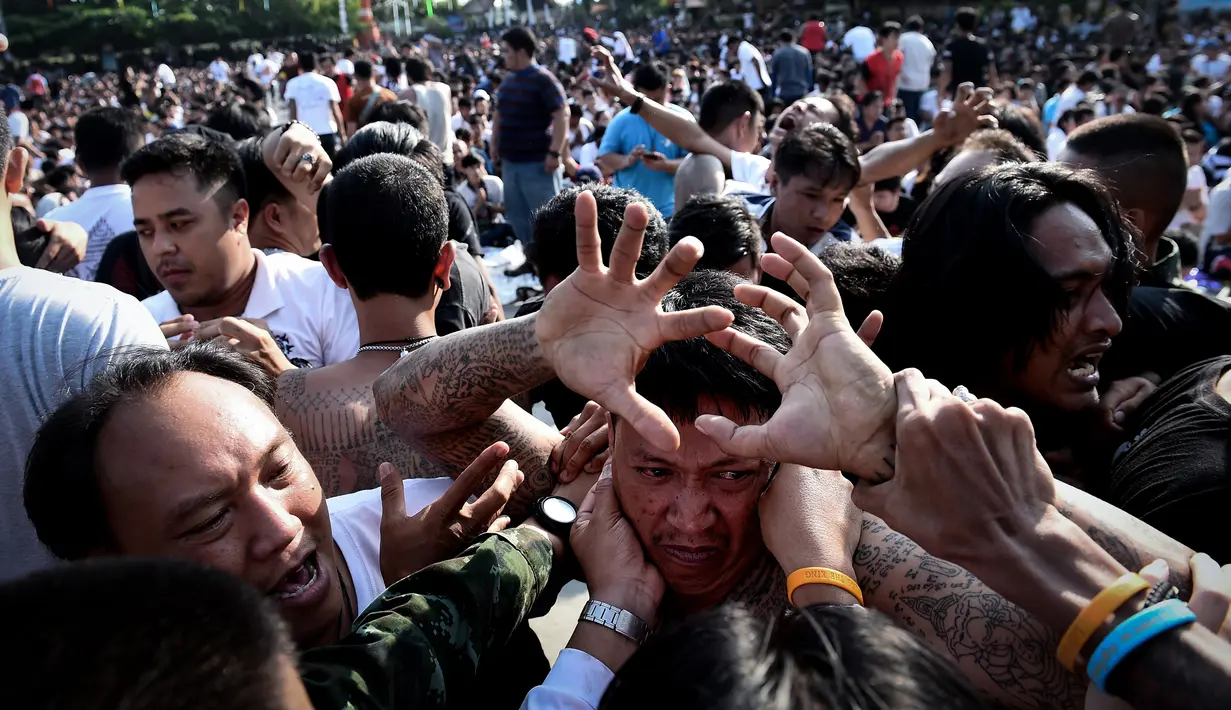 Petugas kemananan setempat dibantu warga menangani pria yang kesurupan saat mengikuti festival tato suci di Biara Wat Bang Phra, Nakhon Pathom, Thailand (3/3). (AFP Photo/Lillian Suwanrumpha)