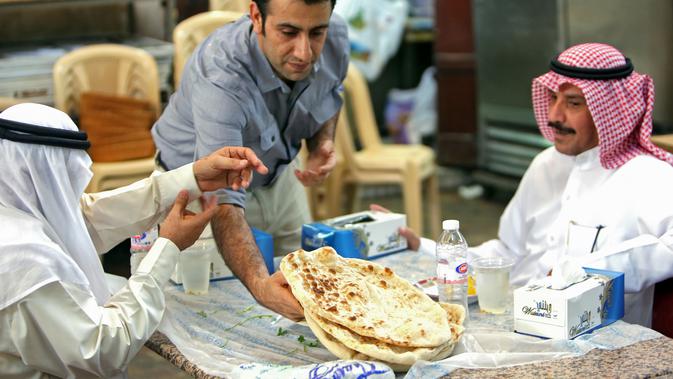Pelayan menyajikan roti Iran atau taftoon kepada pelanggan di sebuah toko di Kuwait City, Kuwait, 27 Juni 2019. Taftoon akan lebih nikmat bila disajikan saat masih panas. (YASSER AL-ZAYYAT/AFP)