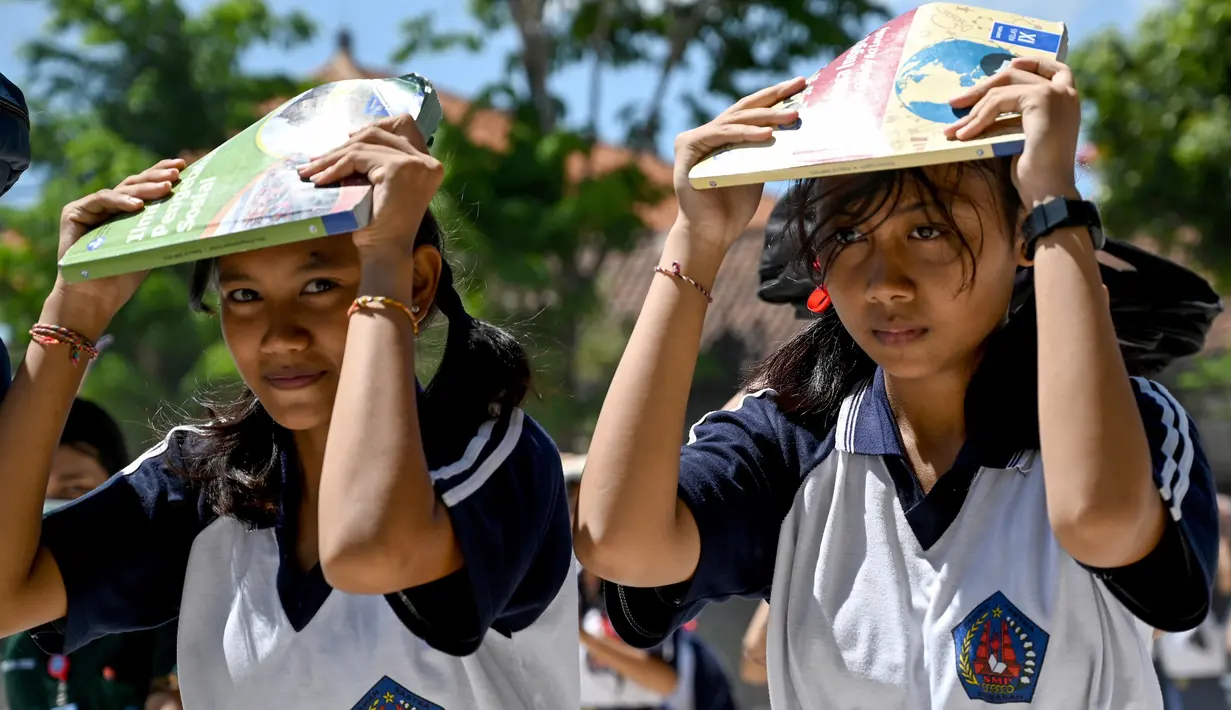Dua siswi saat mengikuti simulasi gempa bumi dan tsunami di Jimbaran, Bali (5/11/2019). Latihan dilakukan untuk memberikan pengajaran kepada siswa agar mengantisipasi bahaya bencana gempa bumi dan tsunami yang bisa datang sewaktu-waktu. (AFP Photo/Sonny Tumbelaka)
