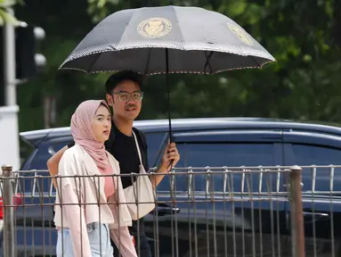 Warga berjalan menggunakan payung di kawasan MH Thamrin, Jakarta, Kamis (21/12/2023). (Liputan6.com/Herman Zakharia)