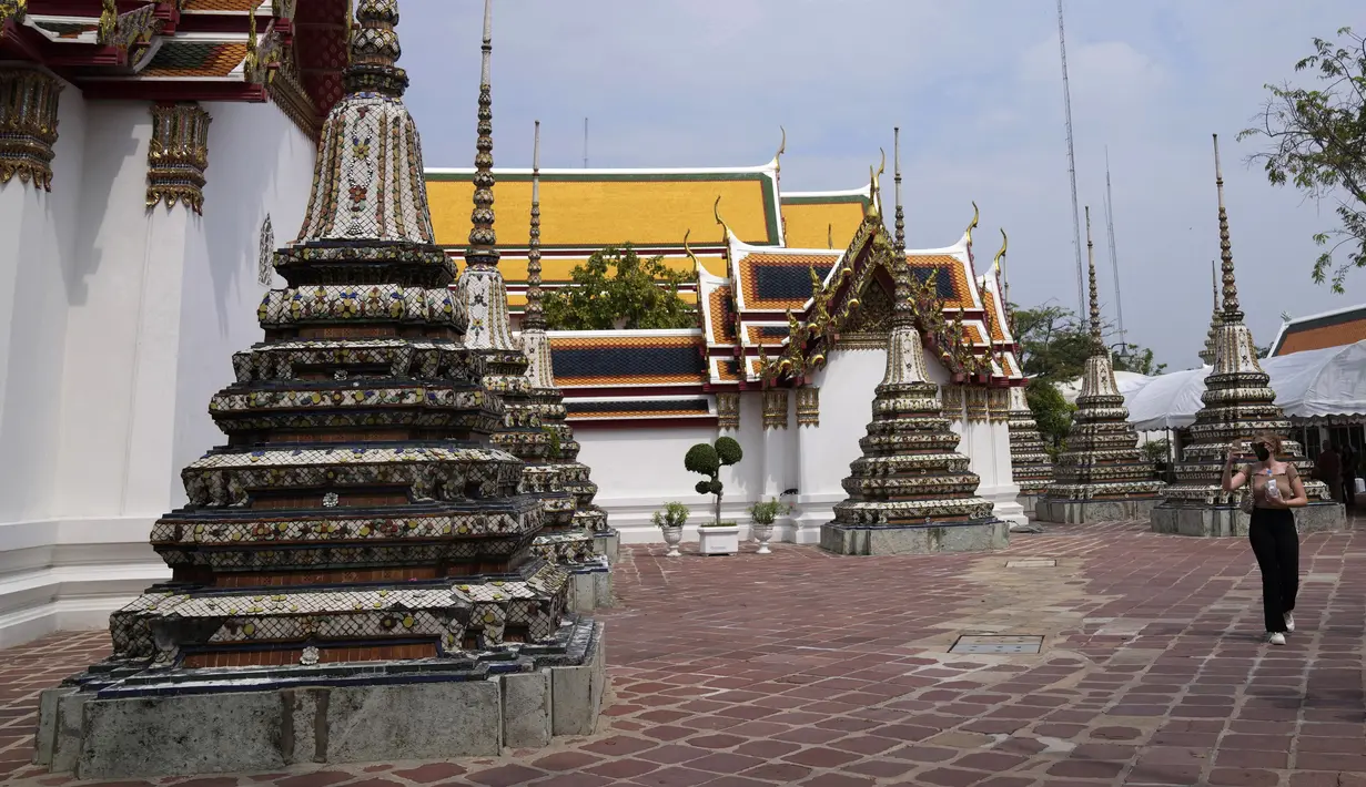 Turis yang mengenakan masker berjalan-jalan di kuil Wat Pho di Bangkok, Thailand, pada 23 Februari 2022. Mulai 1 Maret, turis asing yang telah divaksin penuh hanya diminta menjalani satu kali tes PCR setelah kedatangan dan tes antigen mandiri setelah lima hari. (AP Photo/Sakchai Lalit)