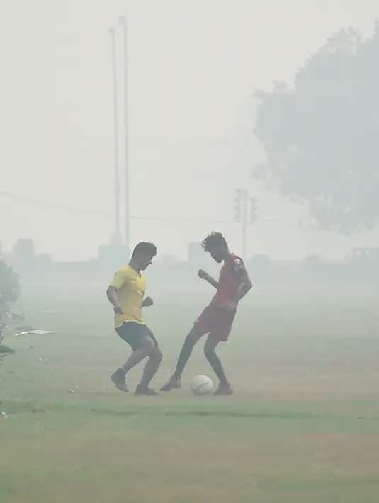 Sejumlah remaja bermain sepak bola dalam kondisi kabut asap tebal di dekat India Gate atau Gerbang India, New Delhi, Selasa (12/11/2019). Kabut asap kembali menyelimuti ibu kota India setelah akhir pekan dengan udara cerah dan cuaca yang lebih baik. (Photo by Money SHARMA / AFP)