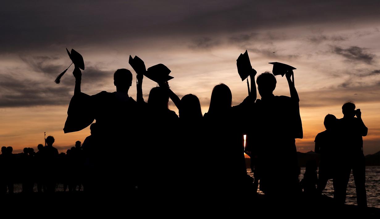 Siswa yang mengenakan gaun kelulusan mereka berpose untuk foto saat matahari terbenam di Victoria Harbour, Hong Kong, Selasa (30/6/2020). (AP Photo/Kin Cheung)