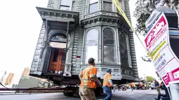 Pekerja melewati rumah bergaya Victoria berusia 139 tahun yang sedang ditarik sebuah truk di jalanan San Francisco, Minggu (21/2/2021). Sepanjang rute, meteran parkir rusak, dahan pohon dipangkas dan rambu lalu lintas dipindahkan. (AP Photo/Noah Berger)