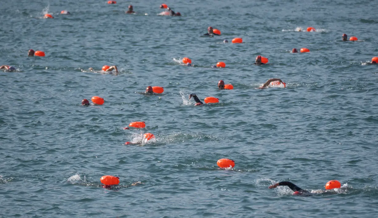 Perenang berenang melintasi Pelabuhan Victoria Hong Kong selama perlombaan renang lintas pelabuhan tahunan di Hong Kong, Minggu (12/12/2021). Namun, di bawah pembatasan covid-19 yang ketat, hanya setengah dari 3.000 perenang biasa yang diizinkan untuk berlomba. (Bertha WANG/AFP)