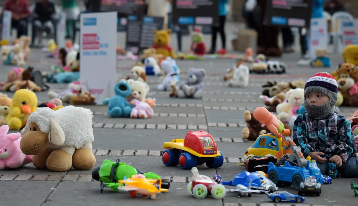 Seorang anak duduk bersama ratusan boneka saat menggelar aksi memprotes penganiayaan terhadap anak sekaligus meningkatkan kesadaran akan tanggung jawab dalam perlindungan anak di Alun-alun Bolivar, Bogota, Kolombia (20/11). (AFP Photo/Raul Arboleda)