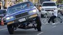 Sebuah mobil Lowrider melaju saat beratraksi dengan roda tiga di Sunset Boulevard, di lingkungan Echo Park, Los Angeles, pada 18 Juli 2021. Lowrider merupakan gaya dari kendaraan modifikasi yang bermula dari Los Angeles pada pertengahan hingga akhir 1940-an. (AP Photo/Damian Dovarganes)