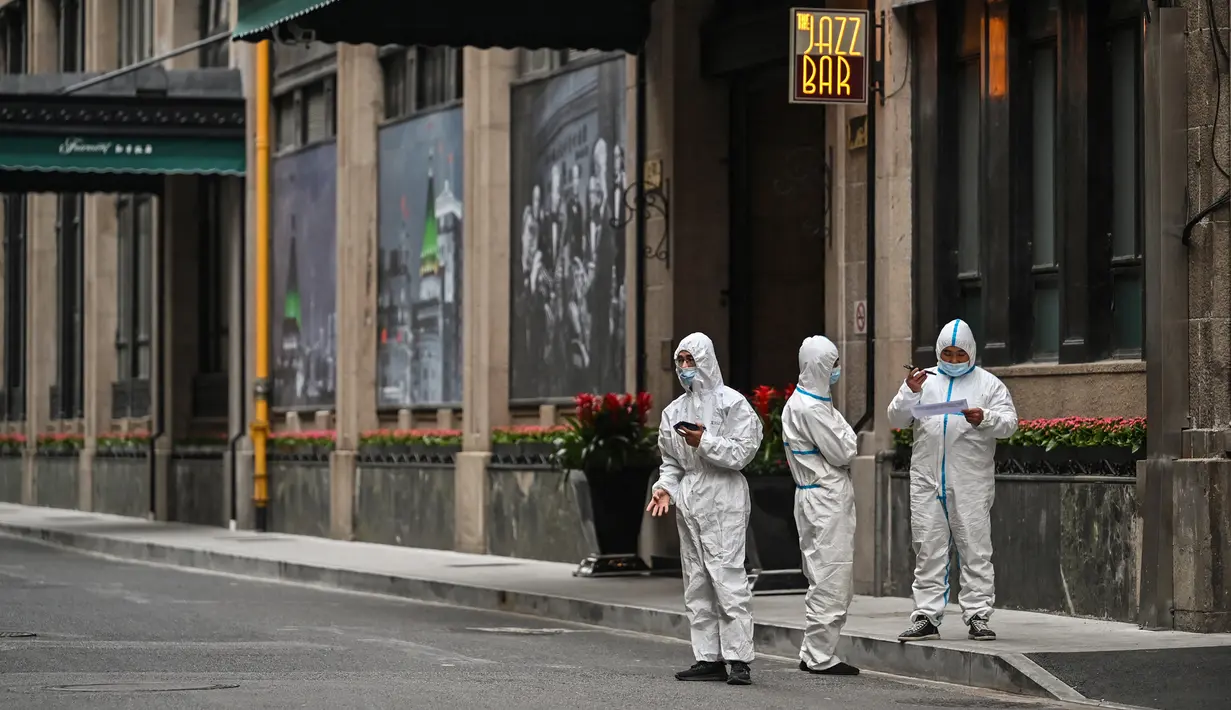 Pekerja yang mengenakan alat pelindung diri dan mengantarkan makanan berdiri di sebelah akses hotel di Bund, Puxi, Shanghai, China, 31 Maret 2022. Daerah Puxi akan lockdown mulai 1 April 2022. (Hector RETAMAL/AFP)