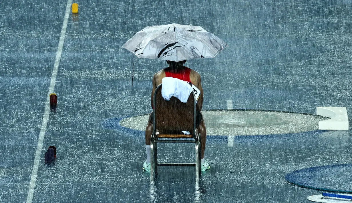 Atlet Thailand, Amsam Ang Patsapong menunggu di bawah payung saat istirahat karena hujan lebat pada final lompat galah putra SEA Games ke-32 di Phnom Penh, Kamboja, 8 Mei 2023. (Photo by MOHD RASFAN / AFP)