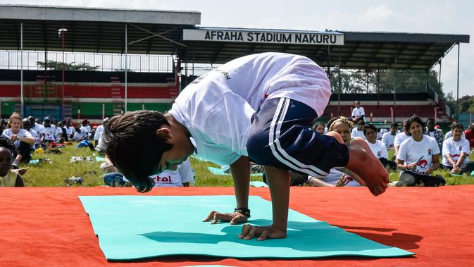 Seorang anak lelaki melakukan gerakan yoga saat mengikuti yoga massal di Stadion Afraha, Nakuru, Kenya (15/6/2019). Hari Yoga Internasional, yang setiap tahun dirayakan pada 21 Juni, pertama kali diusulkan Perdana Menteri India Narendra Modi pada 2014 ke Majelis Umum PBB. (AFP Photo/Suleiman Mbatiah