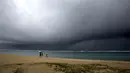 Orang-orang memegang payung saat hujan mulai turun di pantai yang kosong di Honolulu  (6/12/2021). Pihak berwenang mengatakan kondisi yang berpotensi lebih buruk ke depannya. (AP Photo/Caleb Jones)