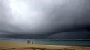 Orang-orang memegang payung saat hujan mulai turun di pantai yang kosong di Honolulu  (6/12/2021). Pihak berwenang mengatakan kondisi yang berpotensi lebih buruk ke depannya. (AP Photo/Caleb Jones)