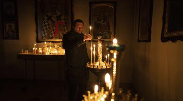Seorang pria menyalakan lilin saat kebaktian Minggu di sebuah gereja Ortodoks di Bucha, di pinggiran Kiev, Ukraina, Minggu, 10 April 2022. Invasi Rusia ke Ukraina hingga saat ini telah berlangsung selama 46 hari. (AP Photo/Rodrigo Abd)