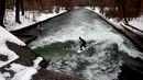 Aksi peselancar menaklukkan ombak saat berselancar di Sungai Eisbach selama hari musim dingin di Munich, Jerman, 4 Januari 2017. Aliran air Eisbach yang memiliki  lebar 12 meter ini berasal dari sungai Isar.  (Mark RALSTON/AFP)