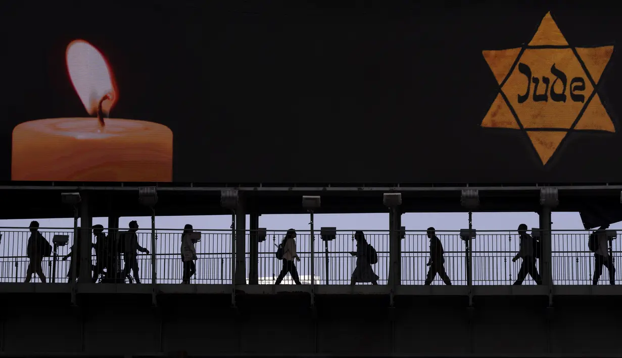 <p>Orang-orang berjalan melewati jembatan yang diterangi dengan papan reklame bergambar Bintang Daud kuning bertuliskan "Jude", Yahudi dalam bahasa Jerman, menyerupai yang dikenakan oleh orang-orang Yahudi di Nazi Jerman saat Hari Peringatan Holocaust tahunan di Ramat Gan, Israel, 28 April 2022. Israel memperingati Hari Peringatan Holocaust tahunan bagi enam juta orang Yahudi yang menjadi korban genosida Nazi selama Perang Dunia II. (AP Photo/Oded Balilty)</p>