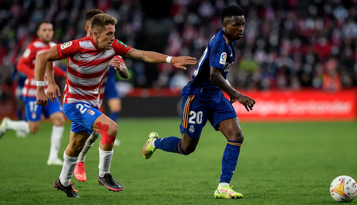 Gelandang Granada Isma Ruiz (kiri) berebut bola dengan pemain depan Real Madrid Vinicius Junior dalam laga lanjutan Liga Spanyol di Stadion Nuevo Los Carmenes, Senin (22/11/2021) dini hari WIB.  Real Madrid menang telak dengan skor 4-1 atas tuan rumah Granada. (JORGE GUERRERO / AFP)