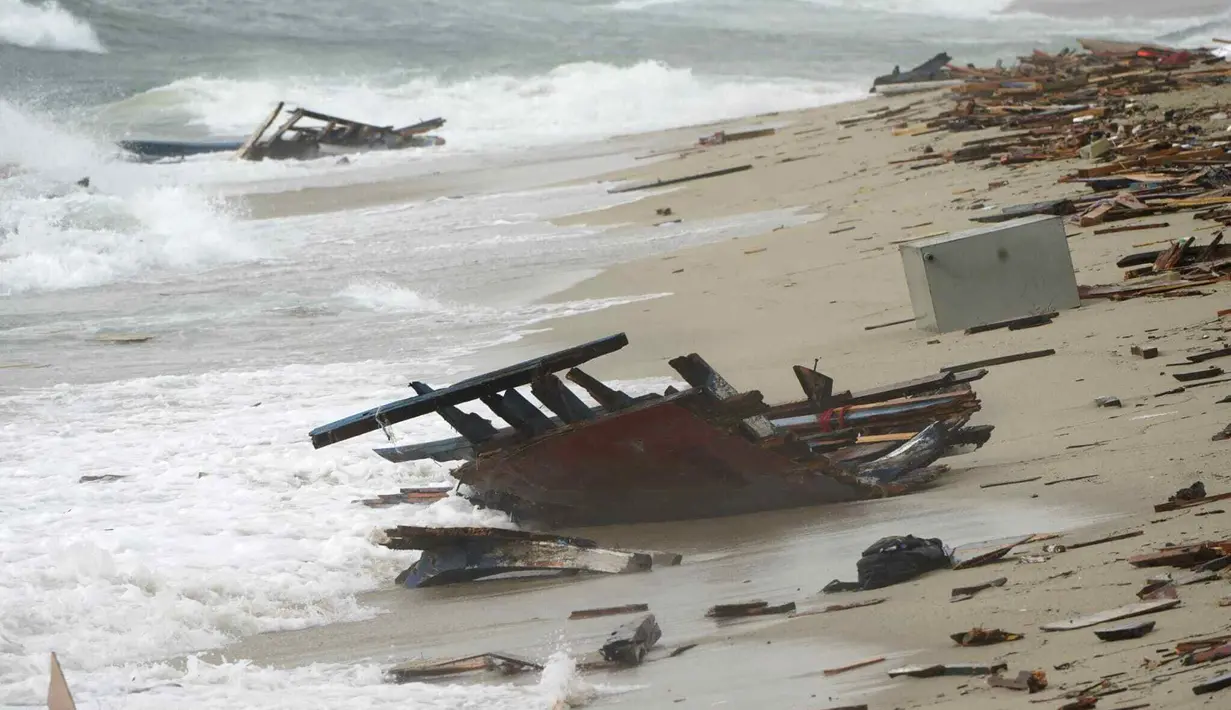Puing-puing kapal terbalik terdampar di pantai dekat Cutro, Italia selatan, Minggu, 26 Februari 2023. Penjaga pantai Italia mengatakan kapal yang kelebihan muatan pecah dalam gelombang keras di lepas pantai Crotone. Seorang petugas melaporkan bahwa seorang tersangka penyelundupan manusia telah ditangkap oleh pasukan keamanan. (Antonino Durso/LaPresse via AP)