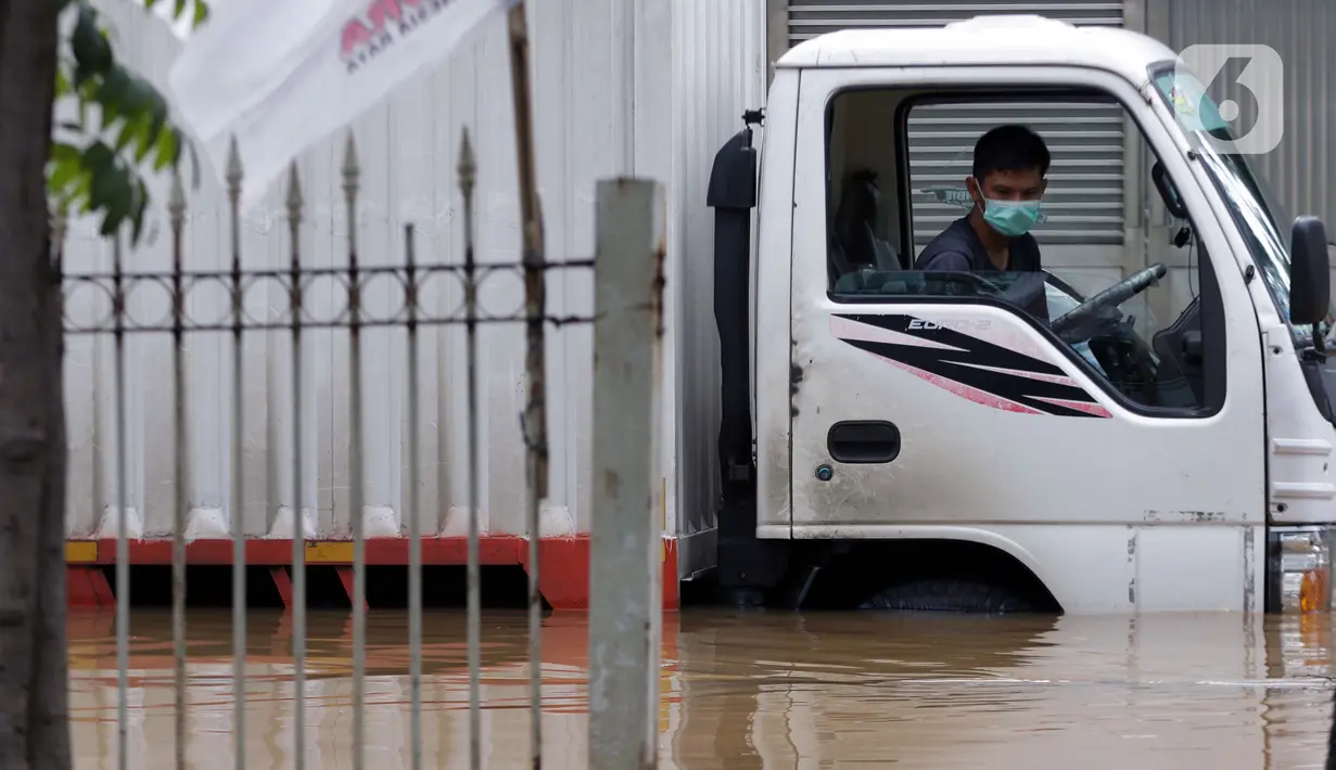 Pengemudi truk duduk dalam kendaraannya saat banjir menggenangi sebagian ruas Jalan Warung Buncit Raya, Jakarta, Sabtu (20/2/2021). Hujan yang mengguyur Jakarta sejak Jumat (19/2) membuat arus lalu lintas sejumlah jalan di Jakarta lumpuh akibat terendam banjir. (Liputan6.com/Helmi Fithriansyah)