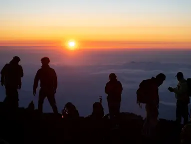 Foto pada 19 Juli 2021 menunjukkan orang-orang menyaksikan matahari terbit dari puncak Gunung Fuji, barat Tokyo. Mendaki Gunung Fuji bukan hal yang mudah, tetapi pemandangan matahari terbit di atas lautan awan adalah hadiah indah bagi yang mencapai puncak tertinggi di Jepang. (Charly TRIBALLEAU/AFP)