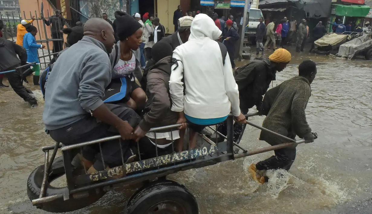 Pejalan kaki menggunakan gerobak melintasi banjir dalam perjalanan ke tempat kerja setelah hujan deras di Nairobi, Kenya (15/3). (AFP Photo/Simon Maina)