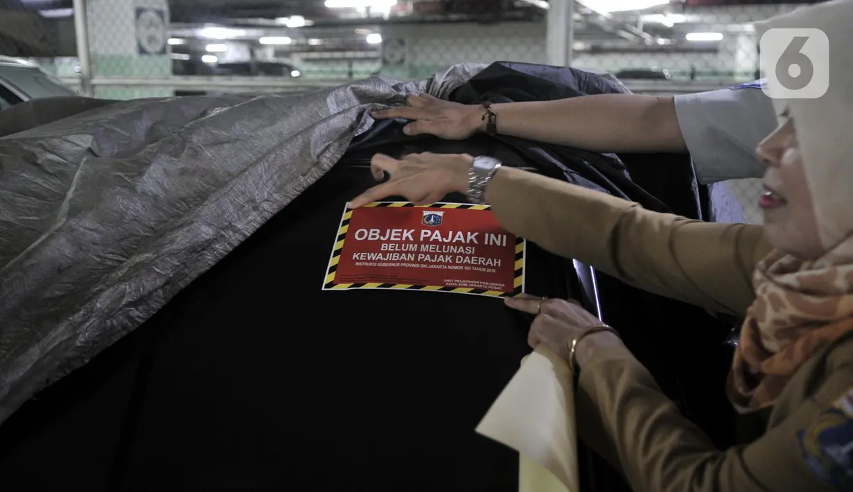 Petugas BPRD DKI Jakarta menempelkan stiker saat razia supervisi pencegahan pajak kendaraan mewah di Apartemen Pavilion, Jakarta, Senin (9/12/2019). BPRD DKI Jakarta bekerja sama dengan Samsat Jakpus dan KPK melakukan penindakan 6 mobil mewah di Apartemen Pavilion. (merdeka.com/Iqbal S. Nugroho)