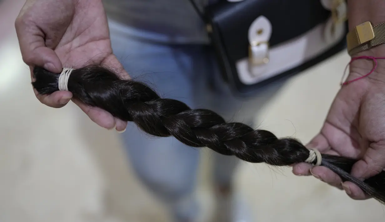 Seorang perempuan menunjukkan sehelai rambutnya setelah dipotong dalam acara Bulan Peduli Kanker Payudara di sebuah mal di Caracas, Venezuela, Sabtu (16/10/2021). Rambut yang dipotong akan disumbangkan untuk membuat wig bagi pasien kanker. (AP Photo/Ariana Cubillos)