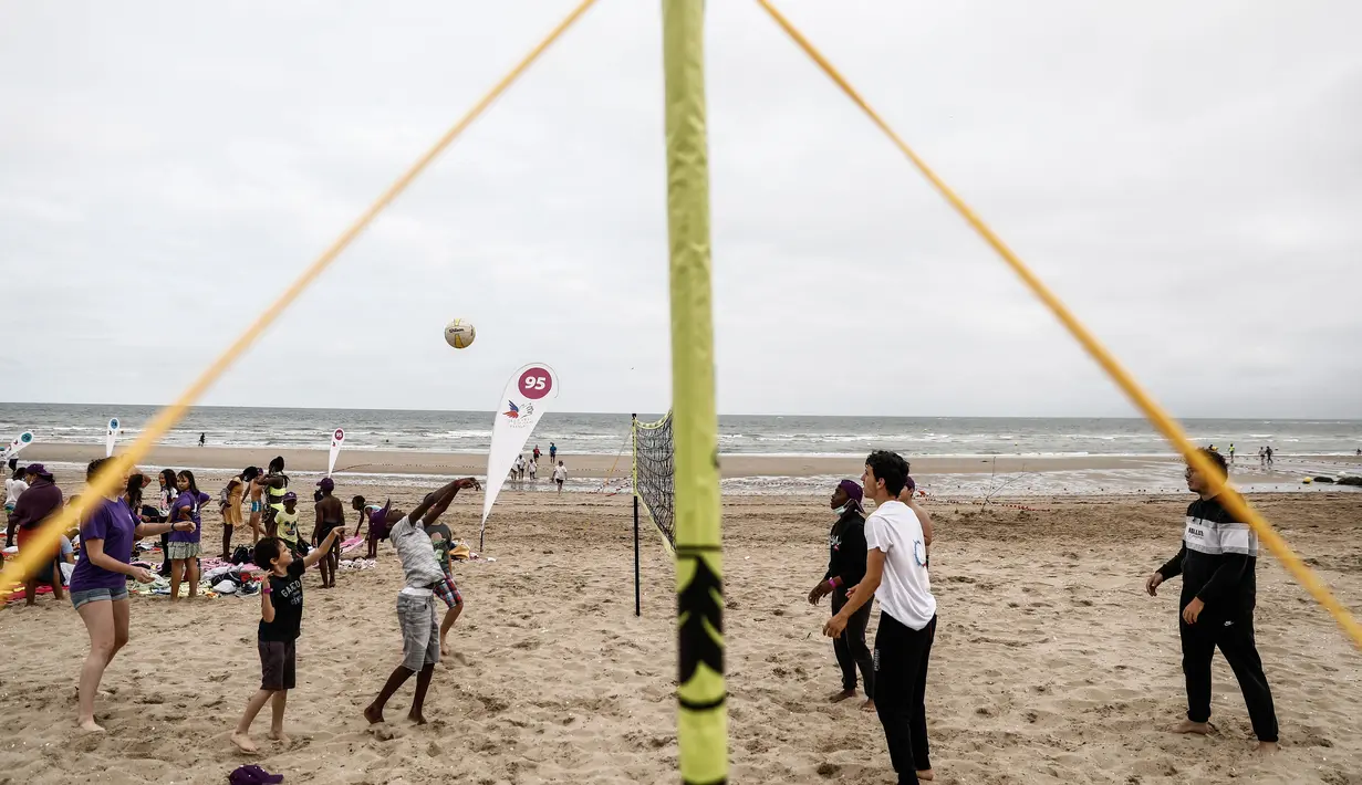 Anak-anak bermain voli pantai di pantai Cabourg, barat laut Prancis (18/8/2021). Seratus bus meninggalkan wilayah Paris dari delapan departemen Ile-de-France dengan 5.000 anak muda dari Ile-de-France dalam situasi genting yang belum sempat berangkat musim panas ini. (AFP/Sameer Al-Doumy)