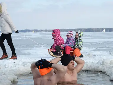 Anak-anak berkereta luncur melewati penggemar renang es di Danau Zalew Zegrzynski di Nieporet, Polandia, Minggu (25/2). Gelombang dingin sedang melanda Polandia. (AP Photo/Alik Keplicz)