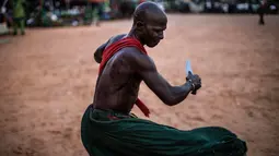 Atraksi seorang warga etnis Joles menggunakan pisau tajam di Bikama, Gambia (24/11). Atraksi ini menunjukan kekuatan sihir yang berasal dari air spritual yang membuat mereka kebal dari senjata tajam. (AFP/Marco Longari)