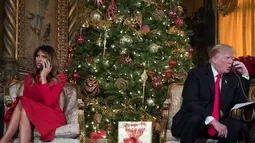 Presiden AS Donald Trump dan Melania Trump saat berbicara dengan anak-anak di telepon di Palm Beach, AS (24/12). Acara ini dibuat untuk menjelaskan keberadaan Sinterklas kepada anak-anak dan mendengarkan permintaan mereka. (AP Photo/Carolyn Kaster)