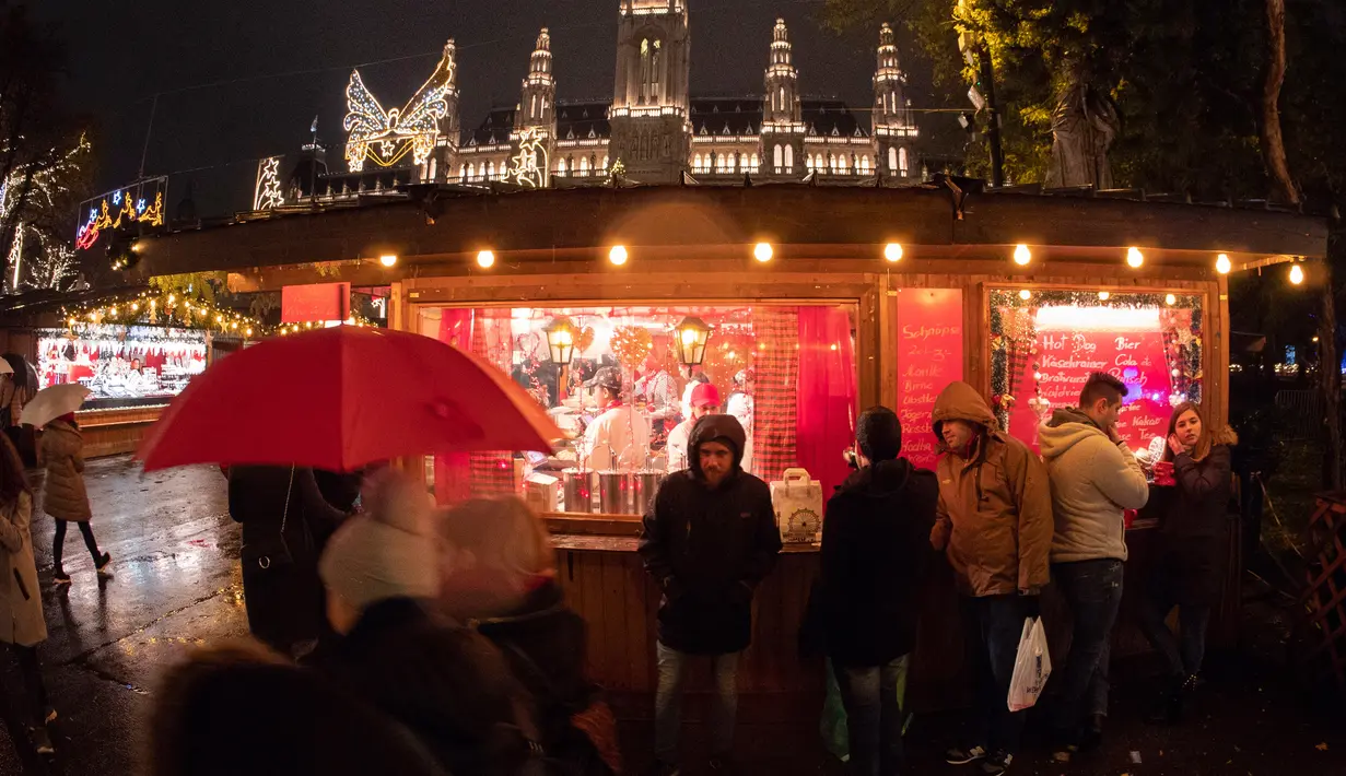 Wisawatan mengunjungi pasar Natal saat hujun turun di luar City Hall, Wina pada 26 November 2018. Di Pasar Natal ini, para pengunjung bisa menikmati jajanan khas hingga pernak-pernik kerajinan tangan asli Austria. (JOE KLAMAR / AFP)
