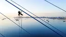 Pekerja menghilangkan es dari kabel Jembatan Russky yang melintasi Selat Bosphorus Timur di Vladivostok, Rusia, Senin (30/11/2020). Lapisan es tebal menutupi pepohonan, mobil, jalan, dan kabel listrik. (AP Photo/Aleksander Khitrov)