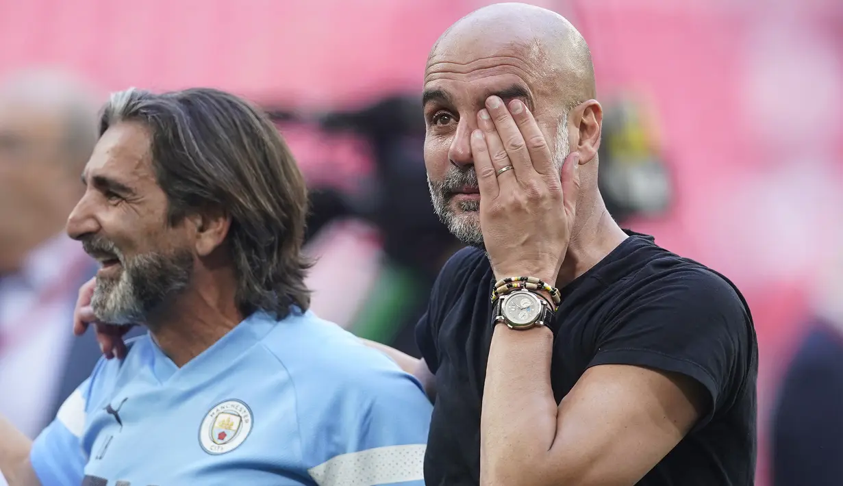 Pelatih Manchester City, Pep Guardiola (kanan), menyeka air matanya setelah berhasil membawa timnya keluar sebagai juara Piala FA 2022/2023 dalam pertandingan final melawan Manchester United yang berlangsung di Wembley, Sabtu (3/6/2023) WIB. (AP Photo/Dave Thompson)
