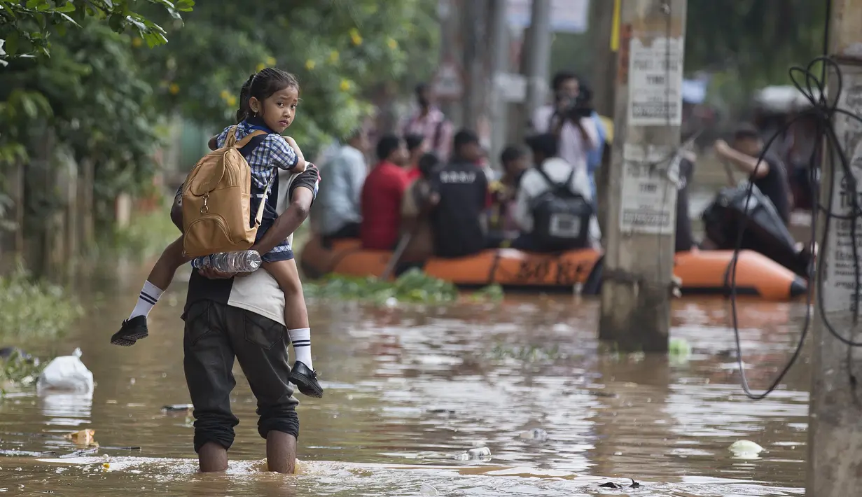Seorang anak diantar ke sekolah saat banjir melanda kawasan Gauhati, India, Rabu (14/6). Angin monsun yang mendatangi India berdampak pada tingginya curah hujan yang menyebabkan banjir. (AP Photo / Anupam Nath)