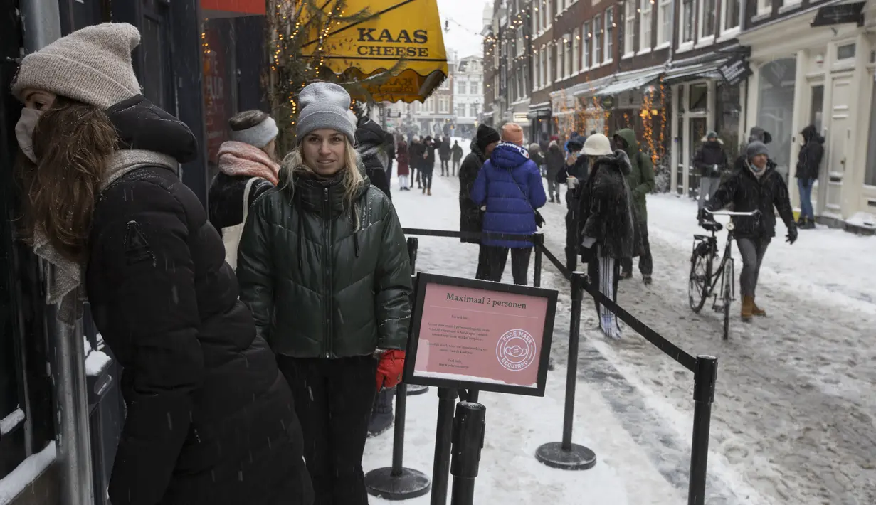 Orang-orang mengantre untuk membeli kue dan kopi di sebuah toko di Amsterdam, karena salju dan angin kencang menyelimuti sebagian besar Belanda, Minggu (7/2/2021). (AP Photo/Peter Dejong)