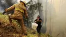 Petugas pemadam dibantu polisi mencoba memadamkan api yang membakar hutan dekat rumah di Sao Joao Latrao, Pulau Madeira, Portugal, Rabu (10/8). Ribuan petugas pemadam dikerahkan untuk memadamkan ratusan titik kebakaran hutan. (REUTERS/Duarte Sa)