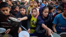 Anak-anak Palestina mendapatkan bagian dari makanan berbuka puasa untuk keluarga mereka di sebuah titik distribusi makanan gratis di kamp pengungsi Nuseirat, Jalur Gaza tengah, pada 14 Maret 2025. (Eyad BABA/AFP)