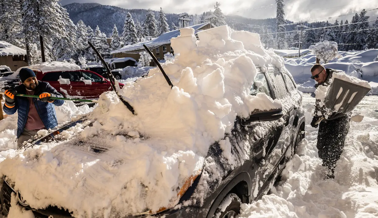 Bryon Wilson (kanan) membantu Shobhit (kiri) menghilangkan salju yang menumpuk pada kendaraan di Tahoe Lakeshore Lodge and Spa, South Lake Tahoe, California, Amerika Serikat, 1 Januari 2023. Badai dahsyat yang menerjang California menyebabkan banjir, pohon tumbang, hingga tanah longsor. (Stephen Lam/San Francisco Chronicle via AP)