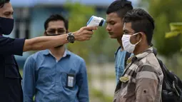 Seorang petugas Urusan Kelautan dan Perikanan Indonesia memeriksa suhu tubuh nelayan Myanmar ketika mereka dideportasi setelah ditahan selama delapan bulan di Banda Aceh (5/8/2020). Mereka ditangkap karena penangkapan ikan ilegal di perairan Aceh sepanjang selat Malaka. (AFP Photo/Chaideer Mahyuddin